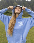 Model holding the hood of the blue Peace Be Still Hoodie outdoors.