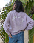 Woman wearing the Vintage Orchid Sweatshirt with blue jeans, showing the Peace of God back graphic