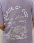 Person wearing a purple t-shirt with a scenic design and text on a beach.