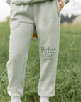 Person wearing light gray sweatpants with 'Perfect Love' text in a grassy field
