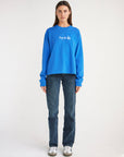 Woman wearing the Strong Blue Pray for Los Angeles long sleeve tee with white chest lettering and dark jeans.