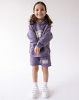 Full-length front view of the Prayer Works kids’ hoodie styled with purple shorts and white sneakers.