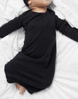 Baby wearing a black outfit and hat lying on a white surface