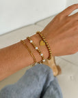 Three Renewal gold-tone bracelets worn together on a wrist beside blue jeans