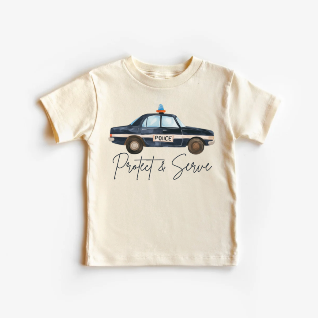A light-colored toddler tee shirt with a graphic of a police car and the text 'PROTECT AND SERVE'.