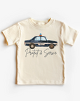 A light-colored toddler tee shirt with a graphic of a police car and the text 'PROTECT AND SERVE'.