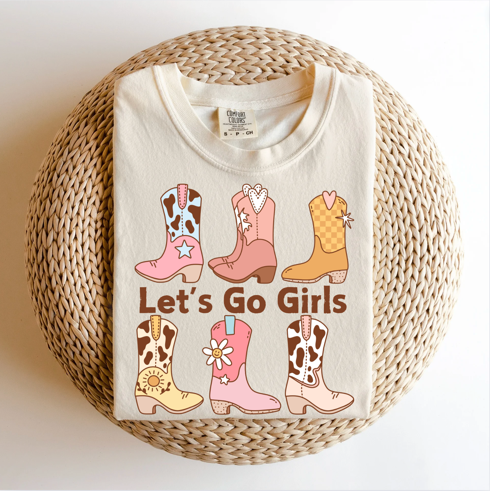 A women's adult t-shirt with a graphic print of cowboy boots and the text 'LET'S GO GIRLS' on a beige background.