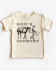 A beige neutral tee shirt top with 'GOD'S COUNTRY' printed in black text and a graphic of a horse and rider in black illustration on the front.