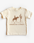 A beige neutral tee shirt top with an illustration of a cowboy on a horse and cactus design.