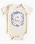 A white bodysuit onesie with blue floral pattern and the text 'new here' printed in the center.