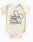 A beige bodysuit with black text and graphic design, depicting a pair of mouse ears and the phrase 'making memories together'.
