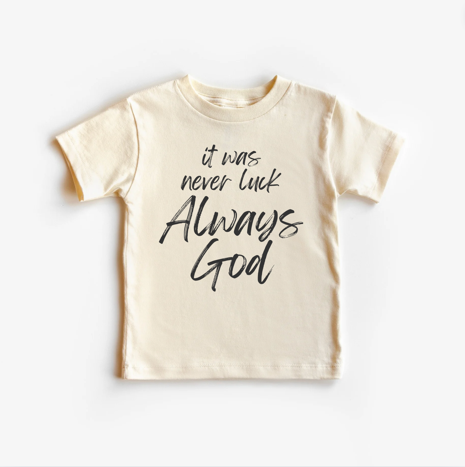 A beige unisex gender neutral tee shirt top with the text 'It was never luck always God' printed on the front.