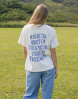 Back view of a model wearing the oversized Spirit of the Lord T-shirt with blue jeans in a grassy field.