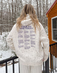 Back view of the ivory Talk to God wildflower hoodie worn outdoors beside a snowy cabin
