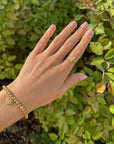 Hand wearing Textured Wrapped Cross Gold-Tone Ring and a bracelet against green foliage