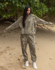 Model wearing The Sacrifice Forest Camo unisex hoodie with coordinating camouflage pants outdoors