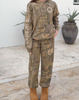 Front view of The Sacrifice camo sweatpants styled with a coordinating hoodie and tan boots.
