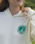Close-up of the Egret hoodie’s small green chest graphic and hood neckline.