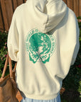 Close-up of the hoodie’s large green globe back graphic outdoors beside a wooden fence.