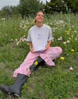 Model seated in a grassy field wearing the Petal Purple Try With God Unisex Tee with pink gingham pants
