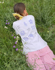 Model wearing the Petal Purple Try With God tee outdoors, showing floral graphics on the back
