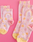 Two pairs of children's socks with rainbows and flowers on a pink background