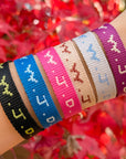Wrist wearing multiple colorful woven bracelets with a blurred red floral background