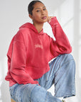 Woman seated wearing Yahweh Ribbon Red Hoodie with small chest lettering and blue jeans