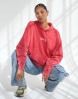 Woman crouching in a Yahweh Ribbon Red Hoodie with relaxed jeans and sneakers