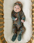 Baby in a patterned outfit lying on a white cushion inside a wicker crib.
