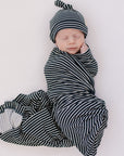 Newborn baby swaddled in a black and white striped outfit with matching hat on a white background