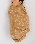 Baby wrapped in a brown blanket with white patterns on a white background