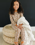 Child sitting on a woven ottoman with a blanket, wearing a patterned outfit against a black background.