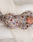 Newborn baby in a floral outfit lying on a white cushion