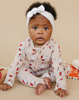 Baby wearing a patterned outfit with a white headband, sitting on a beige surface.