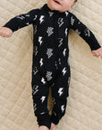 Baby wearing a black onesie with white patterns on a beige quilted surface