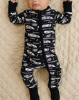 Baby wearing a black and white patterned onesie lying on a beige quilted surface.