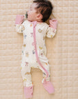 Baby lying on a quilted surface wearing a patterned onesie with pink accents.