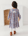 Back view of a girl wearing the blue floral long sleeve dress with a gathered skirt and ruffle hem.