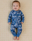 Baby wearing a blue shark print onesie lying on a beige quilted surface