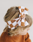 Child wearing a large checkered bow headband with a plain background