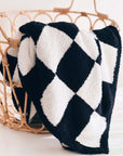 Black and white checkered blanket in a wicker basket on a light background