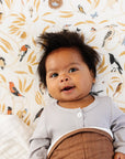 Baby in a crib with a patterned wall and brown blanket