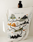 Person holding a large blanket with a map of national parks design on a plain background