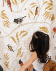 Child sitting on a white floor against a wall with a nature-themed quilt featuring birds and leaves.
