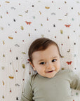 Baby in green ribbed outfit lying on a crib with a patterned sheet