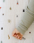 Close-up of a hand wearing a green sleeve against a white fabric background with insect patterns.