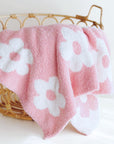 Pink towel with white floral patterns draped over a wicker basket on a white background