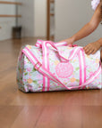 Young girl in a ballet outfit interacting with a floral-patterned duffel bag in a dance studio.