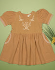 Mustard embroidered puff sleeve dress arranged flat on a green background, showing the front and pockets.